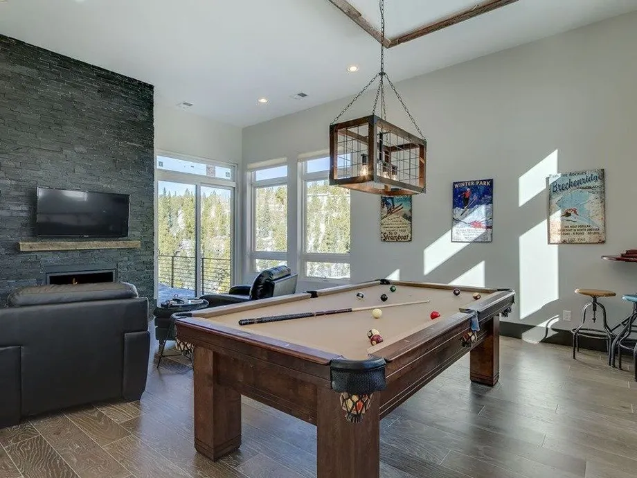 Luxury pool table in a modern game room with natural light, stone wall, and stylish decor, showcasing The Billiard Broker's craftsmanship and design.